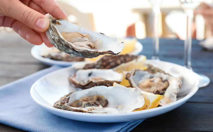 Woman with fresh oyster over plate, focus on hand