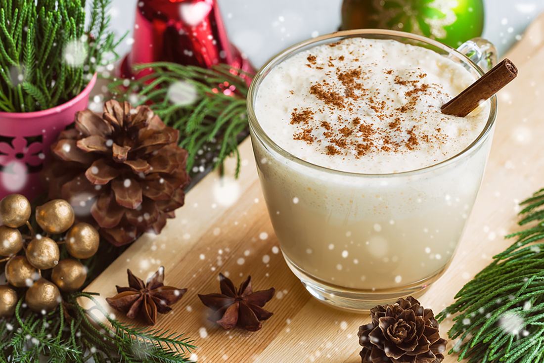 Eggnog traditional drink for Christmas celebration in glass topped with ground nutmeg and cinnamon stick. Homemade eggnog in top view with copy space in Christmas theme and snowfall effect background. Delicious eggnog for Christmas party.